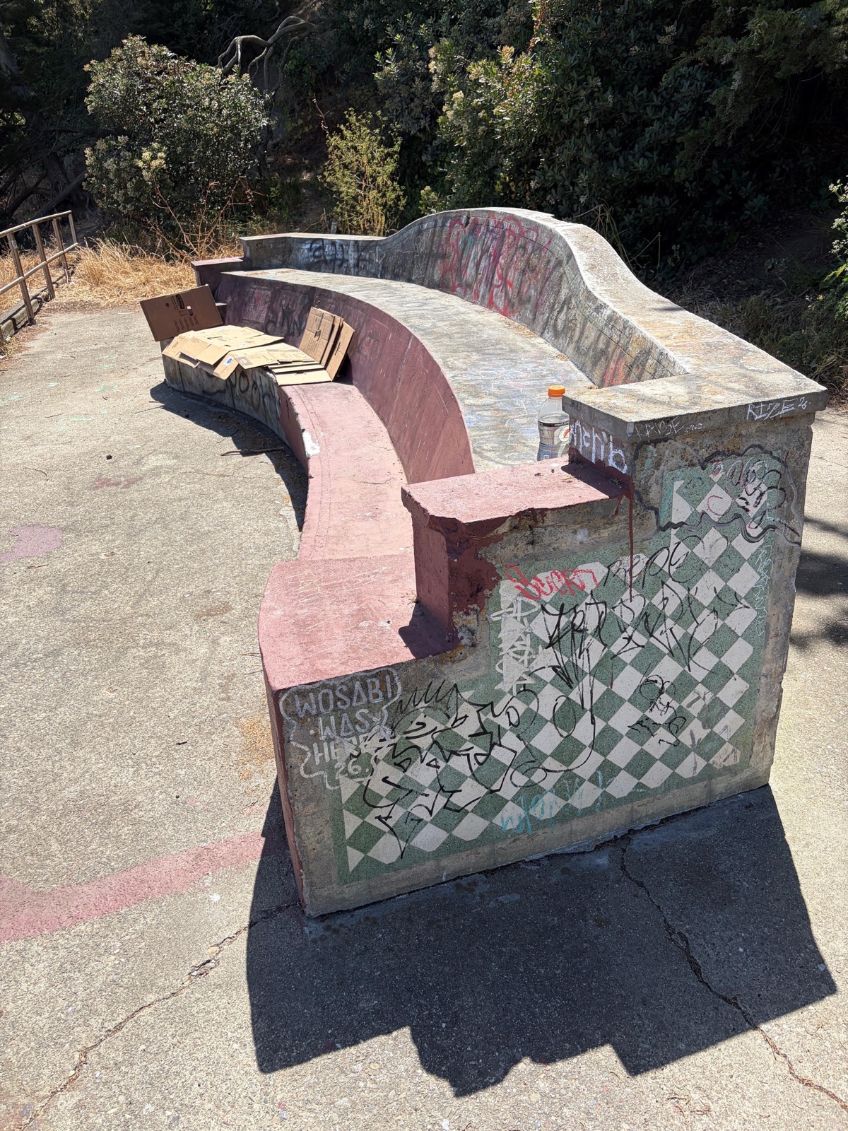 The bench today, showing wear, chipped masonry, and graffiti over its checkerboard tile.
